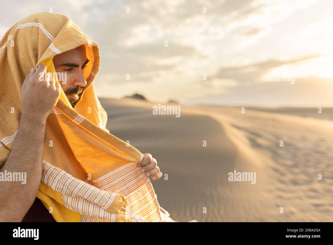 homme dans le désert en expédition avec son visage couvert contre la lumière au coucher du soleil regardant la caméra, dans la lumière dorée, parcourant le monde Banque D'Images