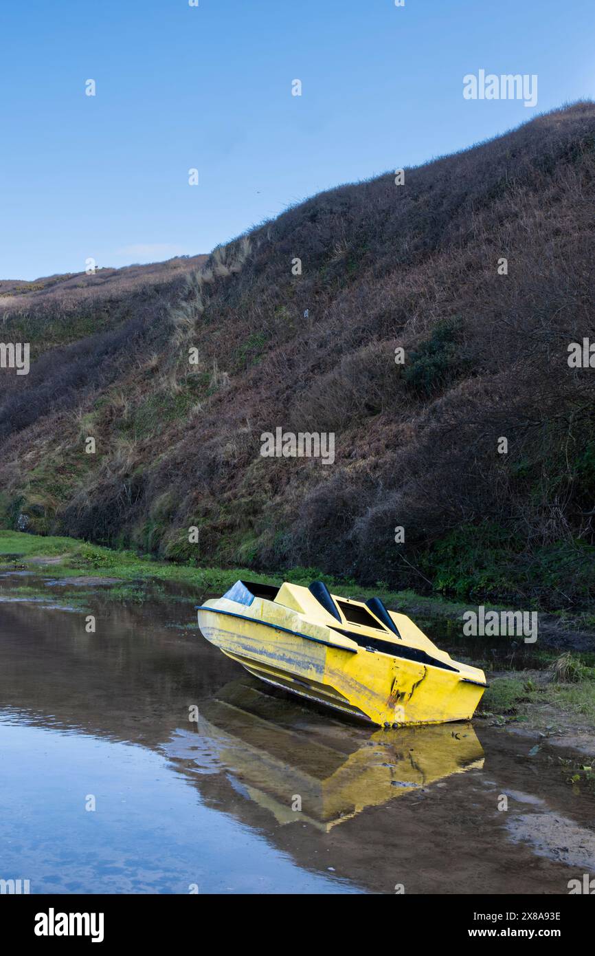 L'épave d'un petit bateau à moteur jaune s'est échouée sur le sentier inondé menant à Crantock Beach sur la côte de Newquay en Cornouailles au Royaume-Uni. Banque D'Images