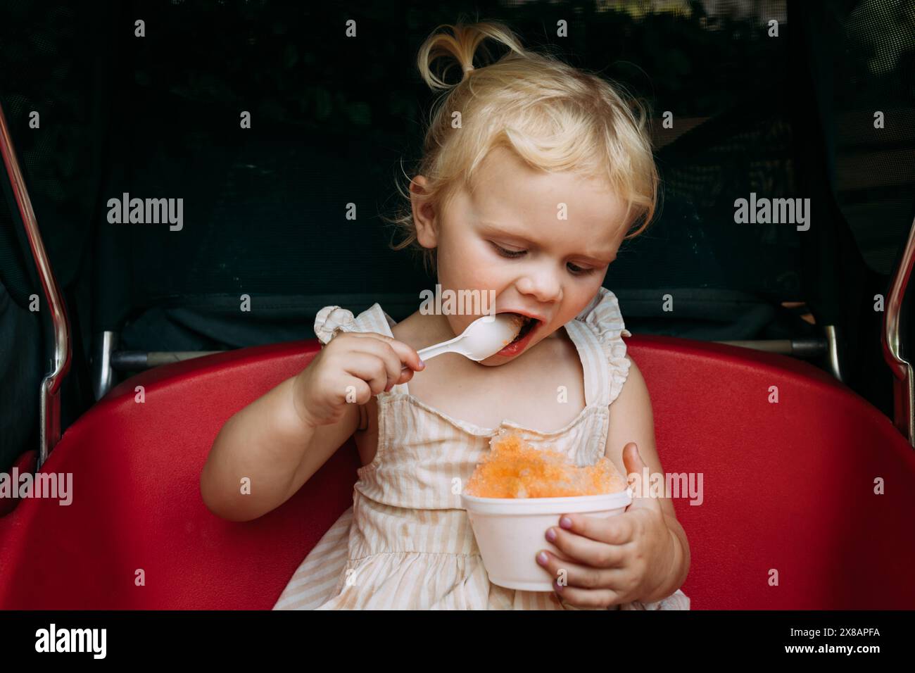 Enfant en bas âge mangeant avec enthousiasme de la glace rasée dans une poussette Banque D'Images