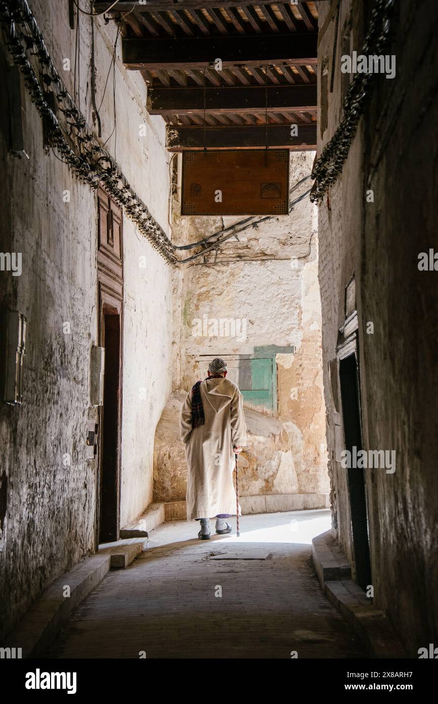 Un homme plus âgé utilise une canne pour marcher dans une ruelle à Marrakech. Banque D'Images