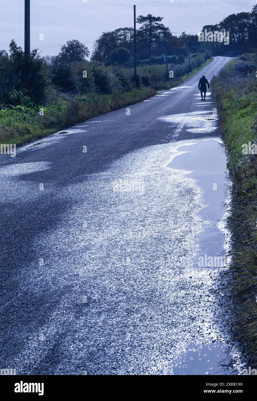 femme solitaire marchant seule sur la route de campagne norfolk angleterre Banque D'Images