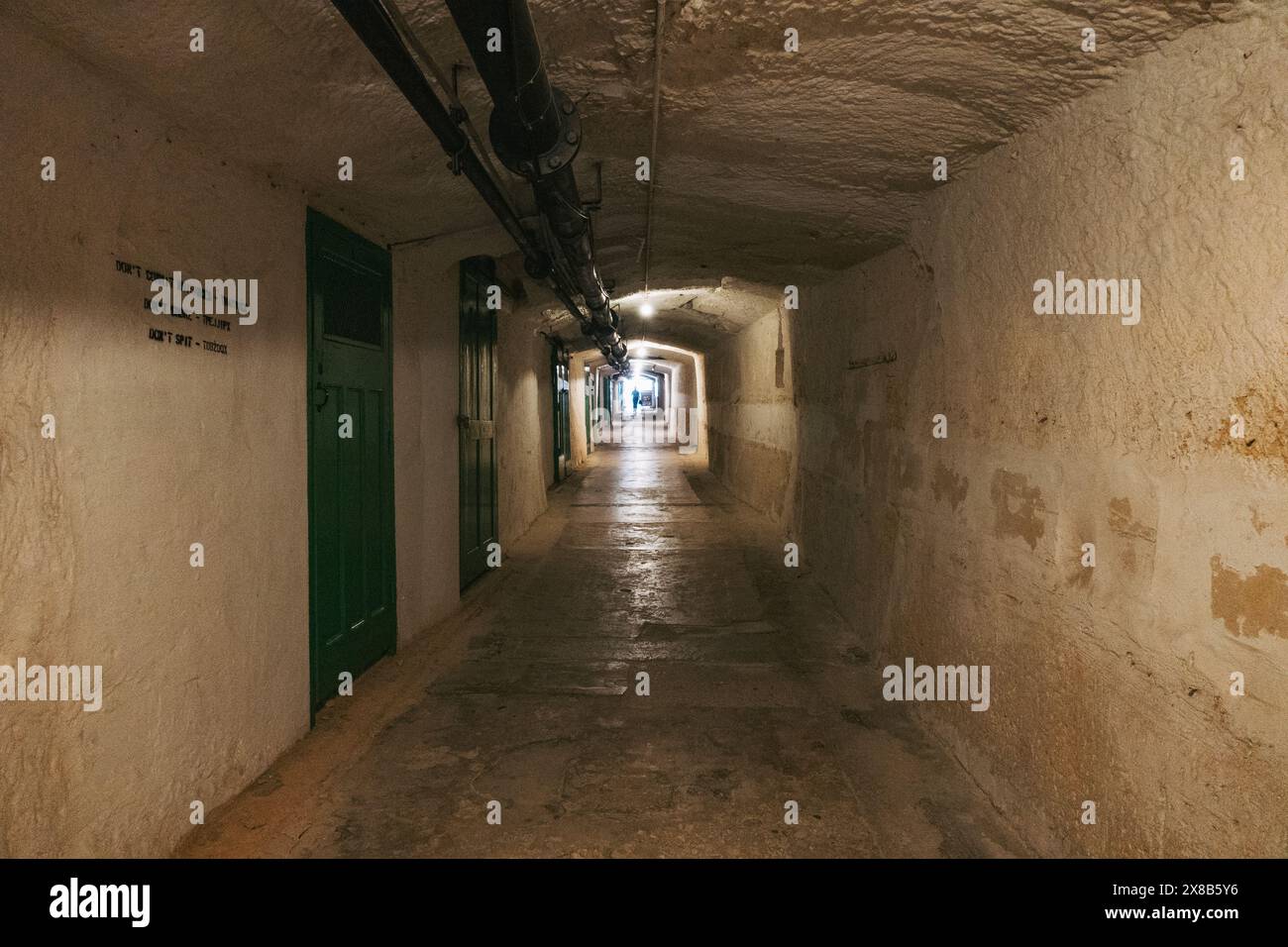 Un long tunnel en pierre avec une porte verte à l'entrée, éclairé par la lumière de l'autre côté, aux Lascaris War Rooms, la Valette, Malte Banque D'Images