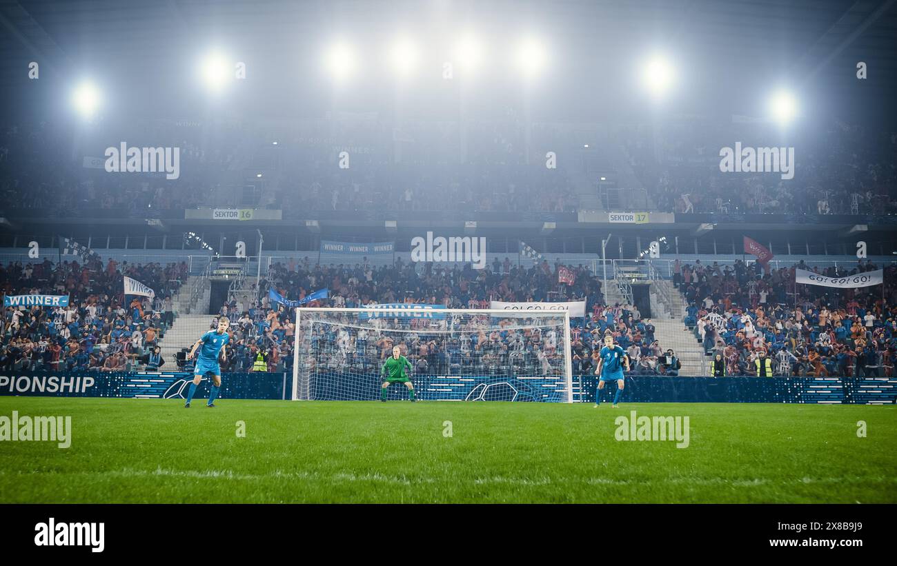 Championnat de football : les joueurs de l'équipe bleue et le gardien de but défendent les objectifs. Prêter une attention particulière aux mouvements adversaires, concentré et prêt à contre-attaquer. Foule de fans acclamations. Banque D'Images