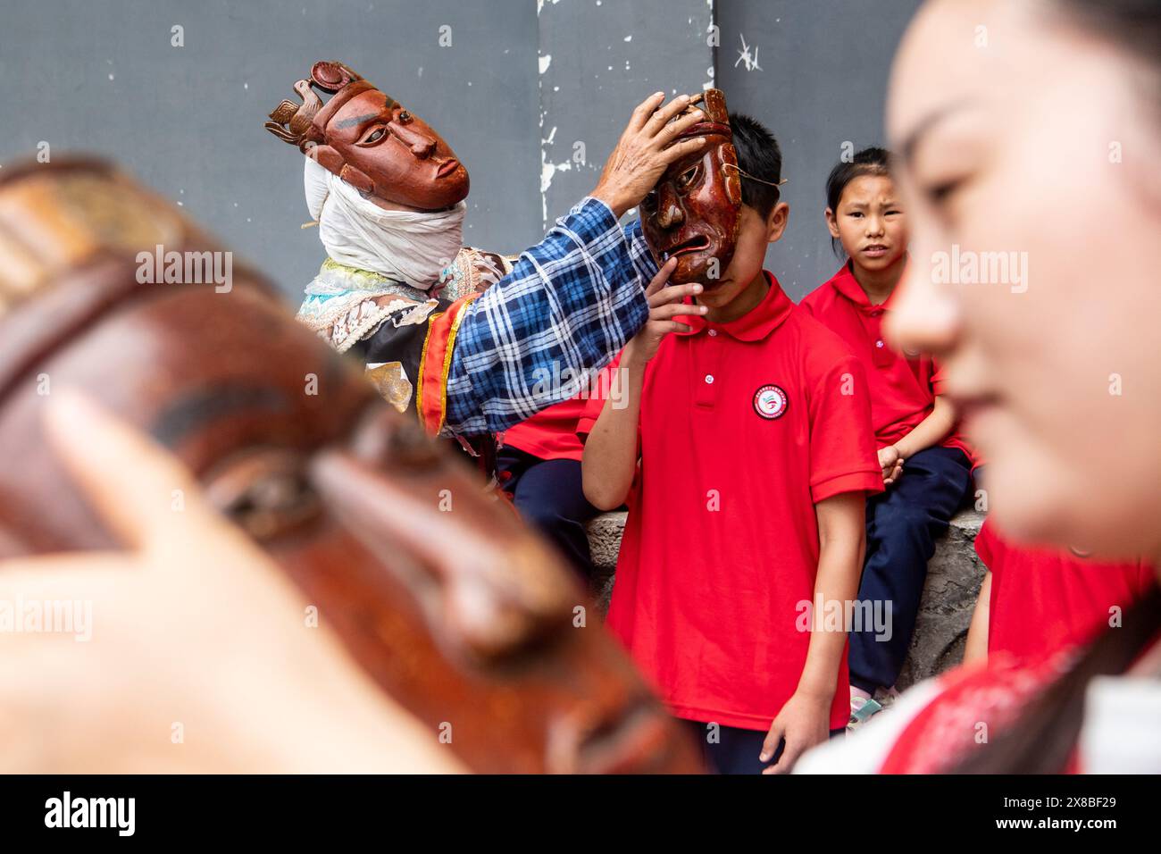 (240524) -- CHONGQING, 24 mai 2024 (Xinhua) -- Un élève d'une école primaire essaie un masque de l'Opéra de Yangxi alors que l'artiste de l'Opéra de Yangxi Chen Yongxia aide à Youyang Tujia et dans le comté autonome de Miao, dans le sud-ouest de la Chine, Chongqing, 17 mai 2024. Dans le village de Qingquan de la municipalité de Tonggu à Youyang, il y a un groupe d'artistes d'opéra composé d'agriculteurs locaux d'une moyenne d'âge de près de 70 ans, qui jouent l'ancien opéra de Yangxi sur les cours et les barrages comme scène, et parmi les rizières, les montagnes et les forêts comme arrière-plan dans le village à environ 1 000 mètres au-dessus du niveau de la mer entouré de moun Banque D'Images