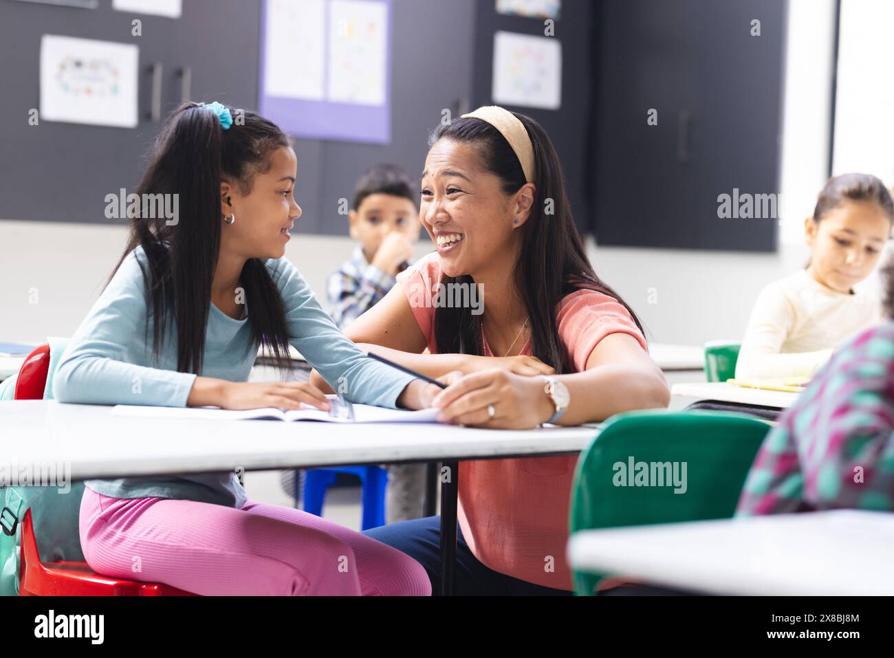 À l'école, une jeune enseignante biraciale parle à une jeune fille biraciale dans la salle de classe Banque D'Images