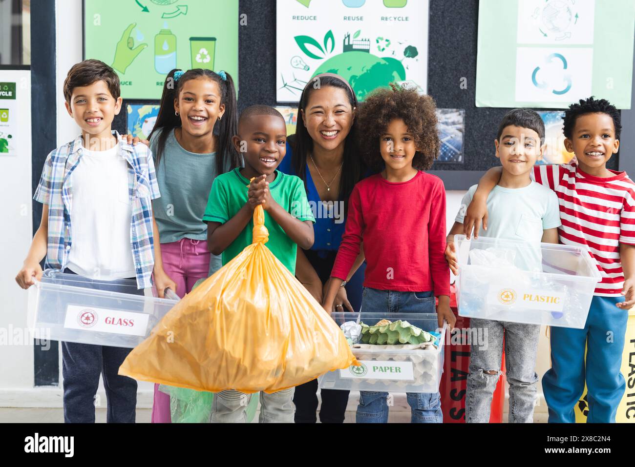 À l'école, un groupe diversifié d'élèves et leur enseignant tenant des matériaux de recyclage dans la classe Banque D'Images