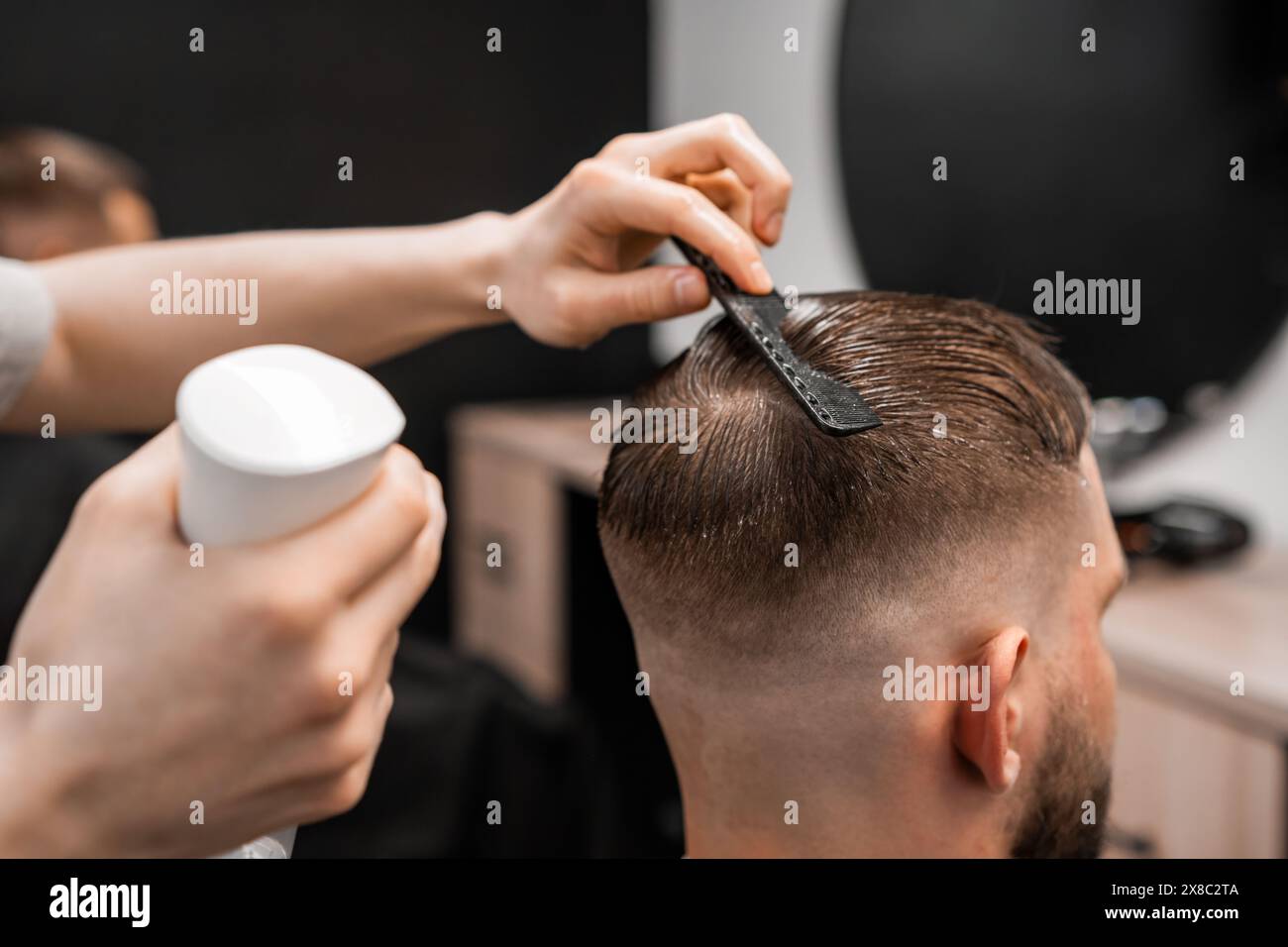 Un barbier pulvérise et peigne les cheveux des hommes au salon de coiffure. Banque D'Images