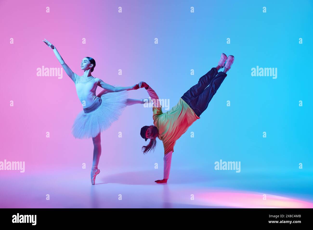 Fusion classique et sport. Belle jeune fille, danseuse de ballet faisant la collaboration créative de danse avec breakdancer sur fond dégradé en néon Banque D'Images