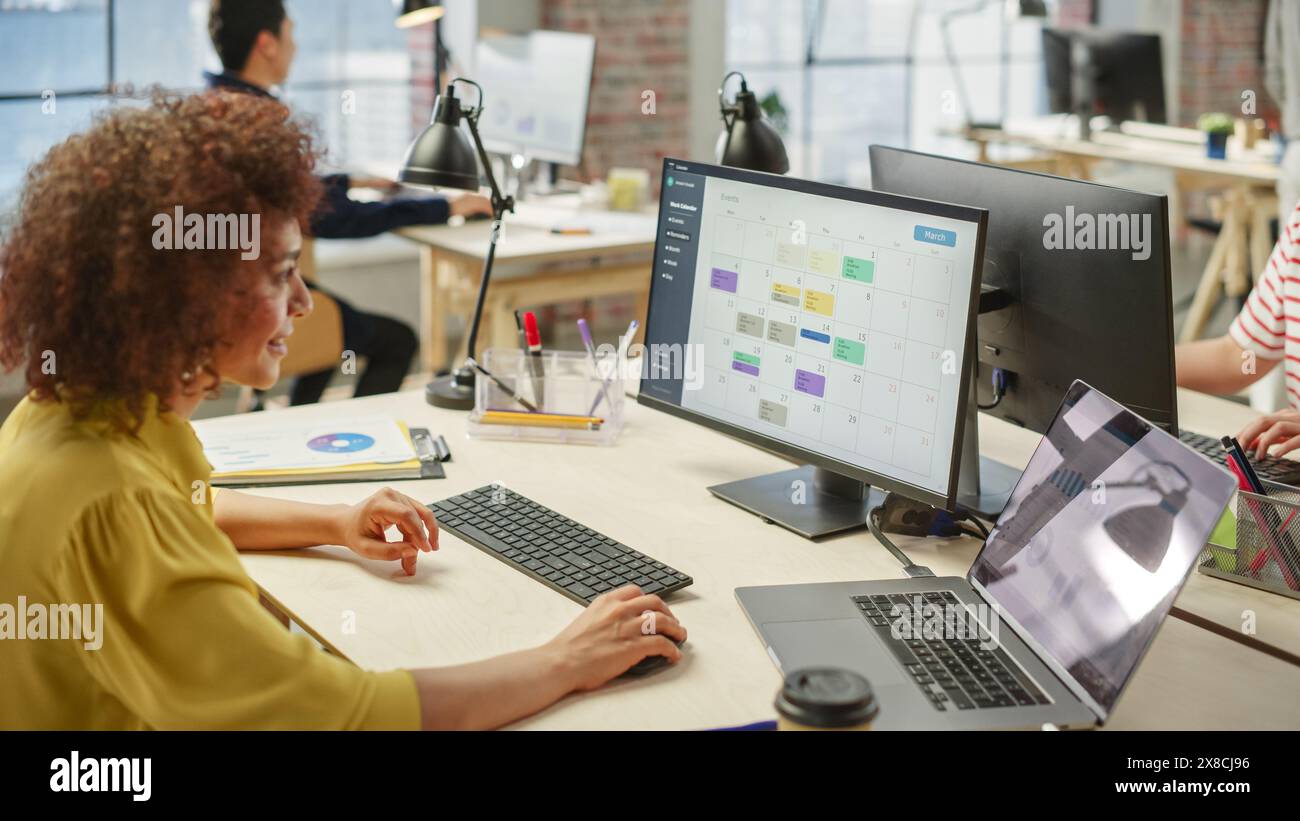 Portrait d'une jeune femme biraciale utilisant l'ordinateur dans un adjoint exécutif occupé travaillant à la planification des réunions. Banque D'Images