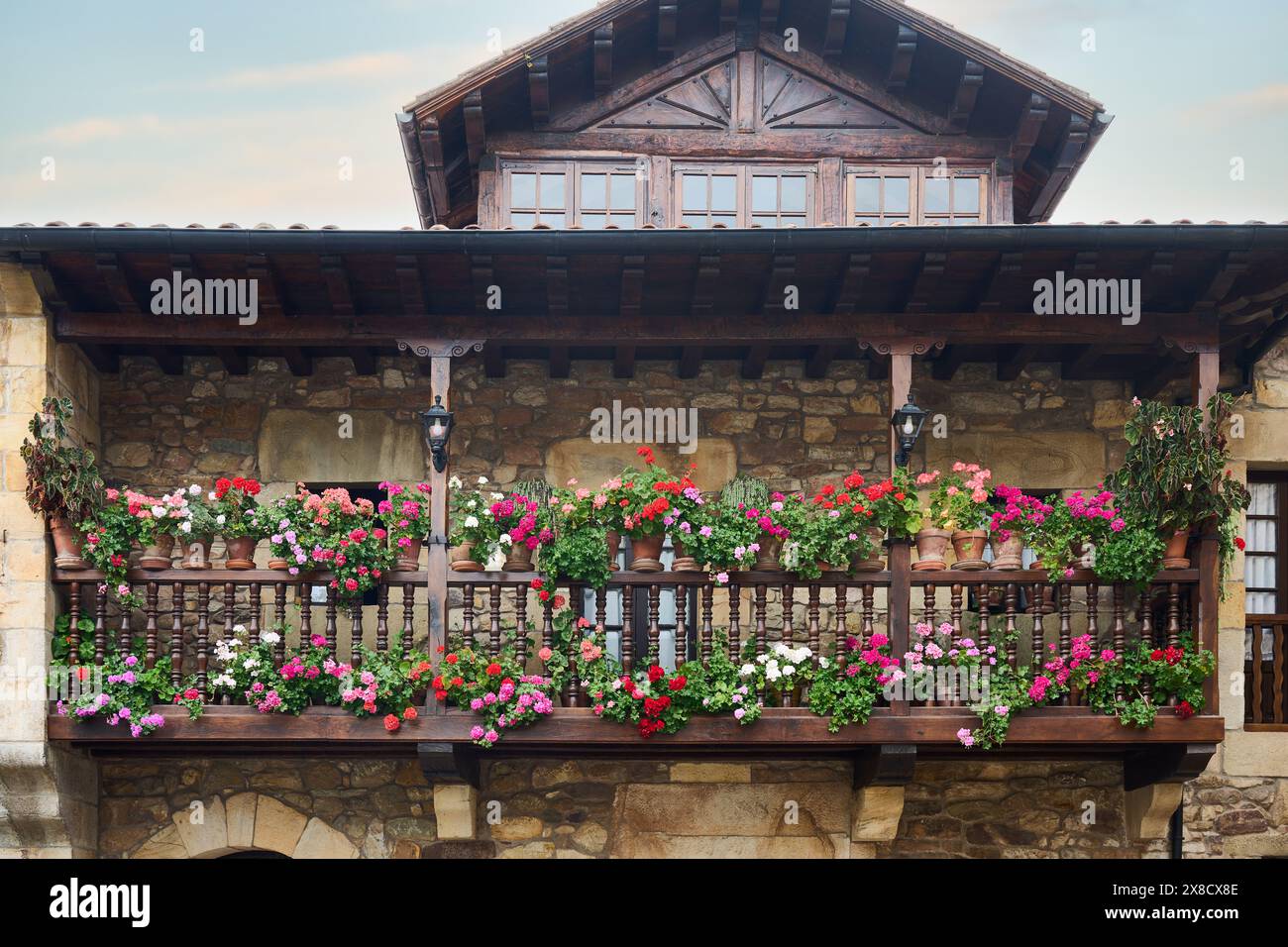 Balcon en bois plein de pots avec des géraniums colorés dans une maison en pierre et bois à cantabrie, Espagne Banque D'Images