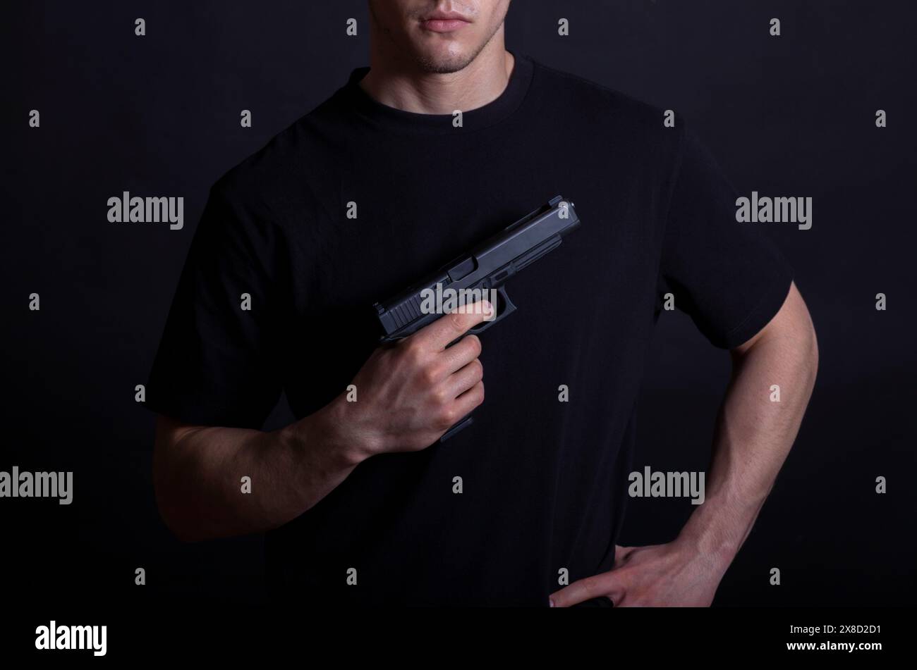 Jeune homme dans un t-shirt noir tenant un pistolet sur un fond sombre Banque D'Images
