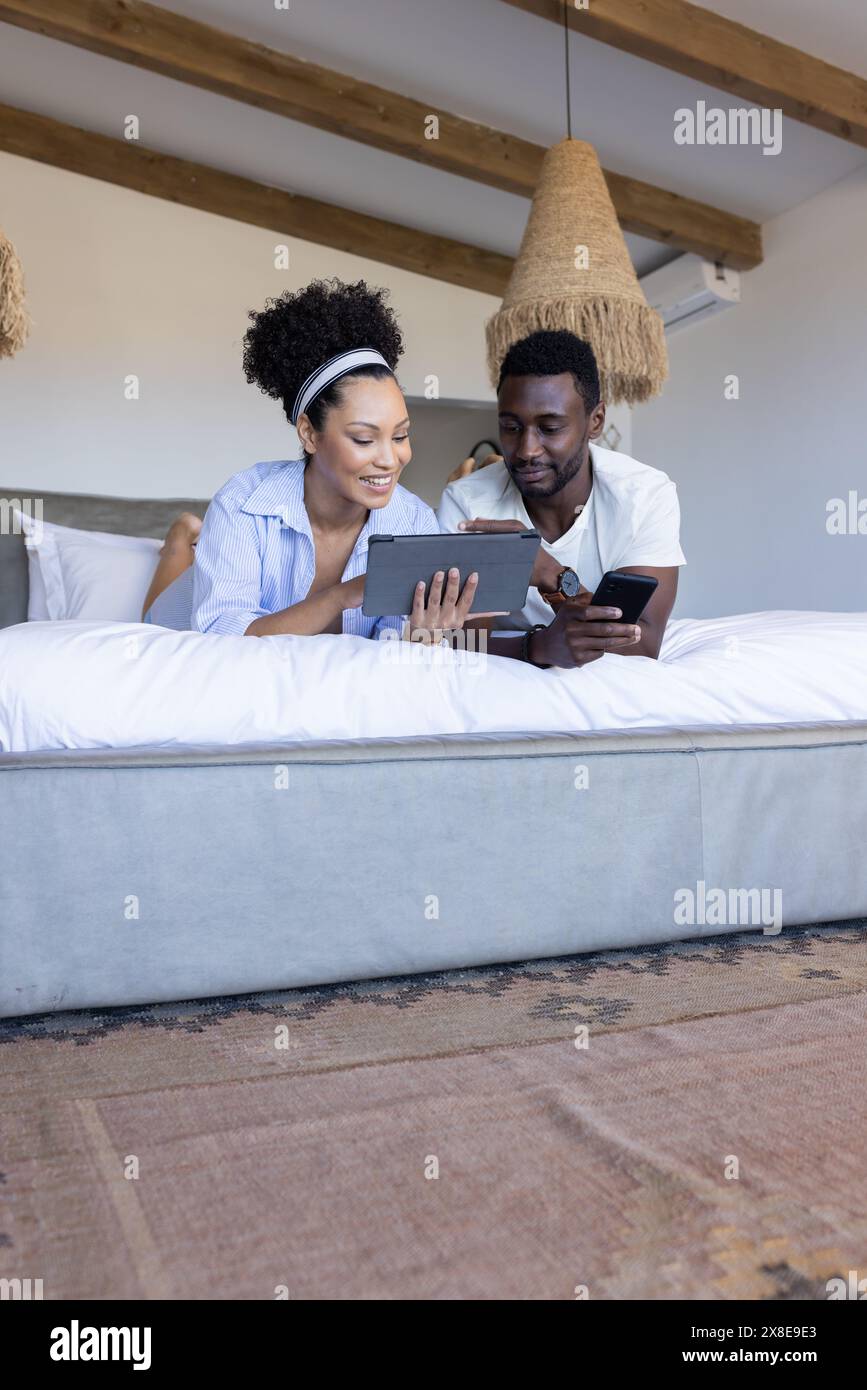 Couple diversifié se relaxant à la maison, regardant tablette et smartphone Banque D'Images
