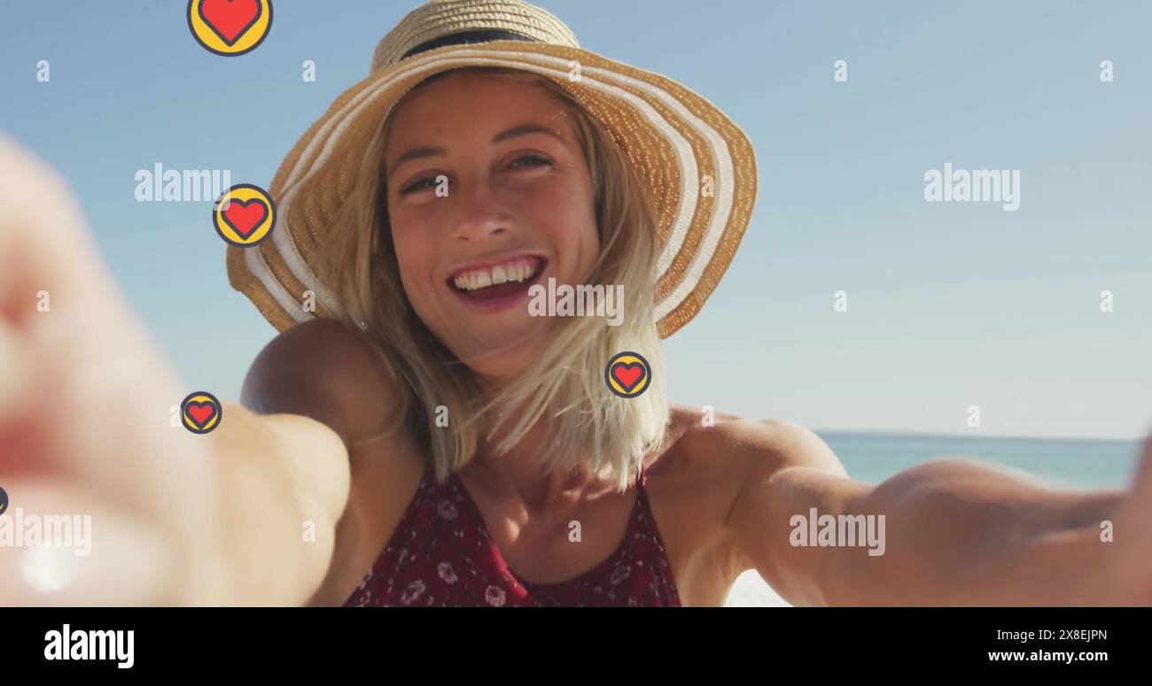 Image d'icônes de forme de coeur, belle femme caucasienne tenant la caméra et enregistrant à la plage Banque D'Images