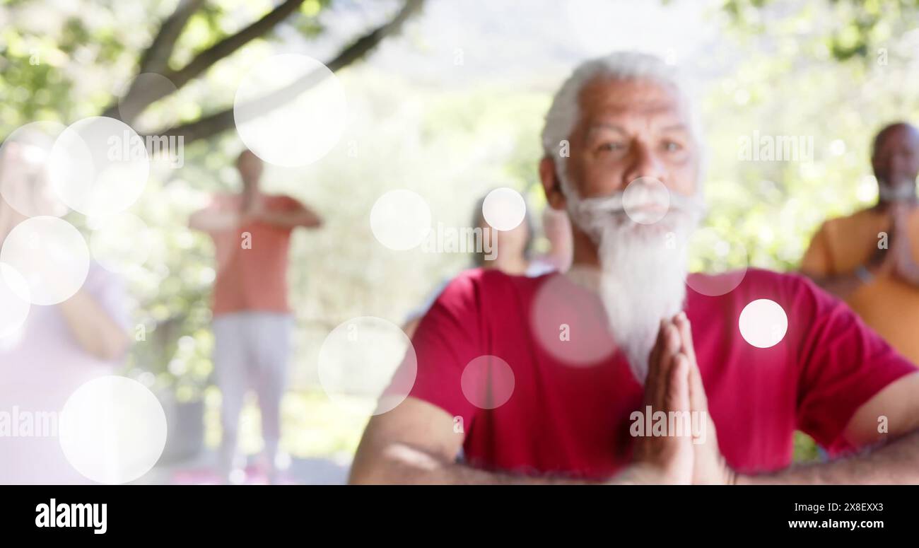 Image de taches de lumière et d'arbres sur diverses personnes âgées pratiquant le yoga dans le jardin Banque D'Images