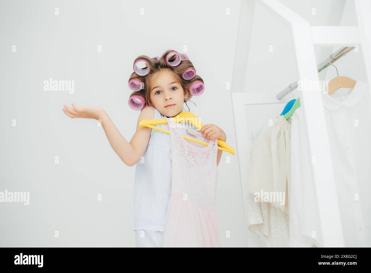 Petite fille avec des rouleaux de cheveux, indécis sur des robes, se préparant pour une journée de fantaisie. Banque D'Images