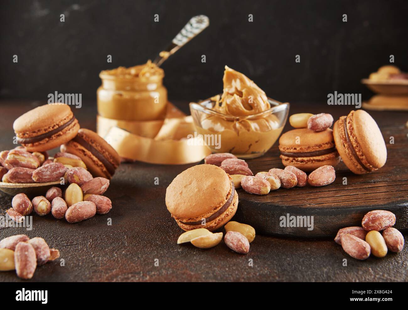 Un pot de beurre d'arachide, un aliment de base, est placé à côté des macarons et des cacahuètes sur la table. Ces ingrédients peuvent être utilisés dans diverses recettes de cuisine Banque D'Images
