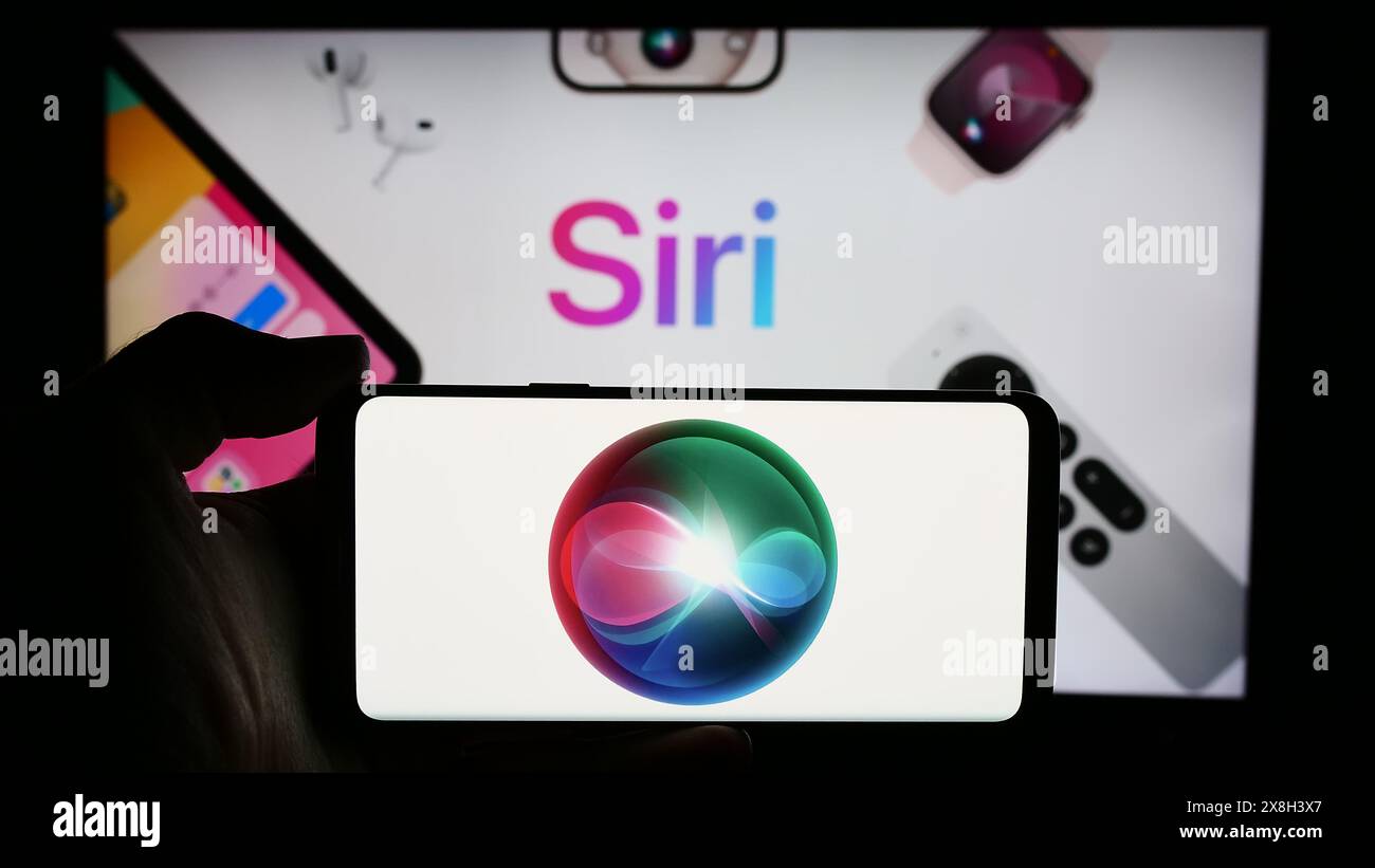 Personne tenant le téléphone portable avec le logo du logiciel assistant numérique Siri (Apple Inc) en face de la page Web de l'entreprise. Concentrez-vous sur l'affichage du téléphone. Banque D'Images