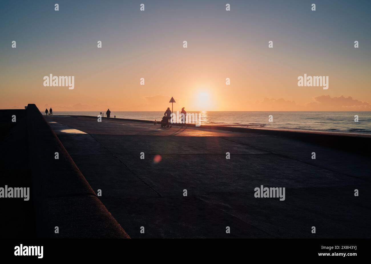 Une soirée paisible au bord de la mer avec des gens marchant sur la promenade, profitant du beau coucher de soleil sur l'horizon. Banque D'Images