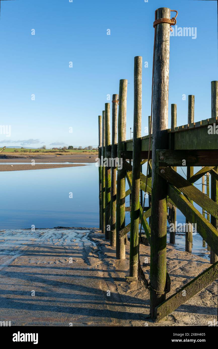 Jetée en bois sereine au-dessus d'un lac tranquille, jour clair, reflets bleus vibrants du ciel, verdure lointaine en arrière-plan Banque D'Images