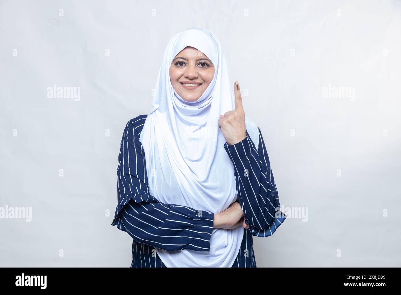 Election en inde. Portrait d'une femme musulmane heureuse portant le hijab montre le doigt marqué avec de l'encre après avoir voté debout isolé sur fond blanc Banque D'Images