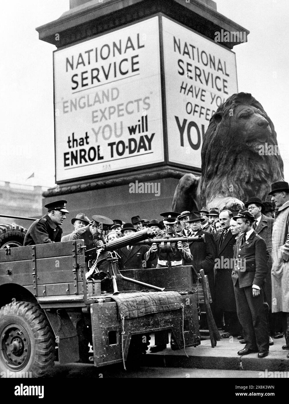 Photo de DOSSIER EN NOIR ET BLANC datée du 05/09/39 de personnes regardant des soldats manifester une mitrailleuse Vickers et un télémètre sous une affiche pour le service national à Trafalgar Square, dans le cadre d'une grande campagne de recrutement au début de la seconde Guerre mondiale. Les adolescents ne seraient pas envoyés en prison pour avoir défié le service national «obligatoire» proposé par les conservateurs, James a habilement dit, car le Labour a qualifié cette politique de «gadget». Date d'émission : dimanche 26 mai 2024. Banque D'Images