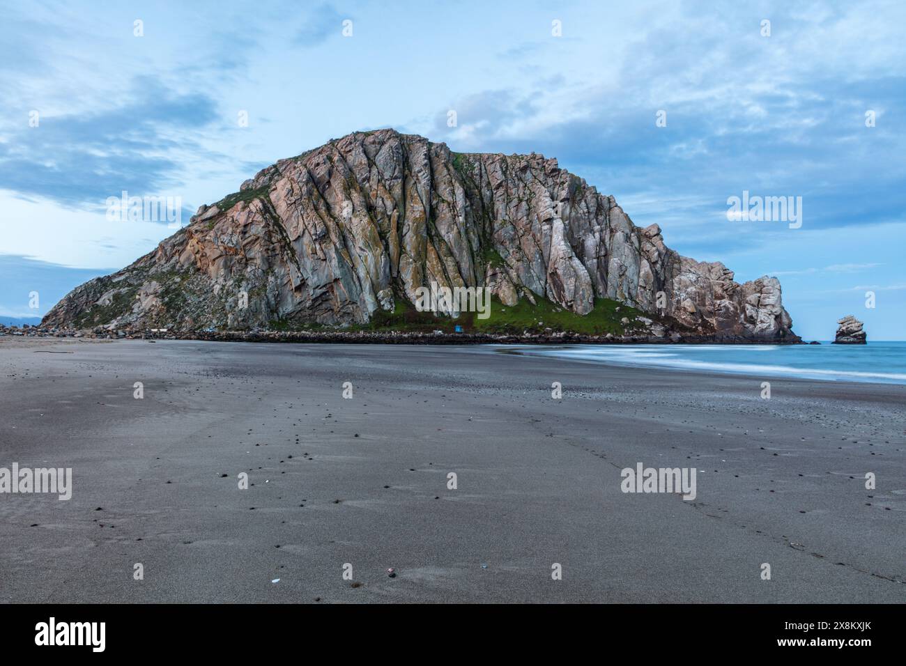 Panorama du célèbre Morro Rock à l'aube, Morro Bay, Californie. Plage de sable au premier plan ; océan à droite. Ciel bleu nuageux au-dessus. Banque D'Images