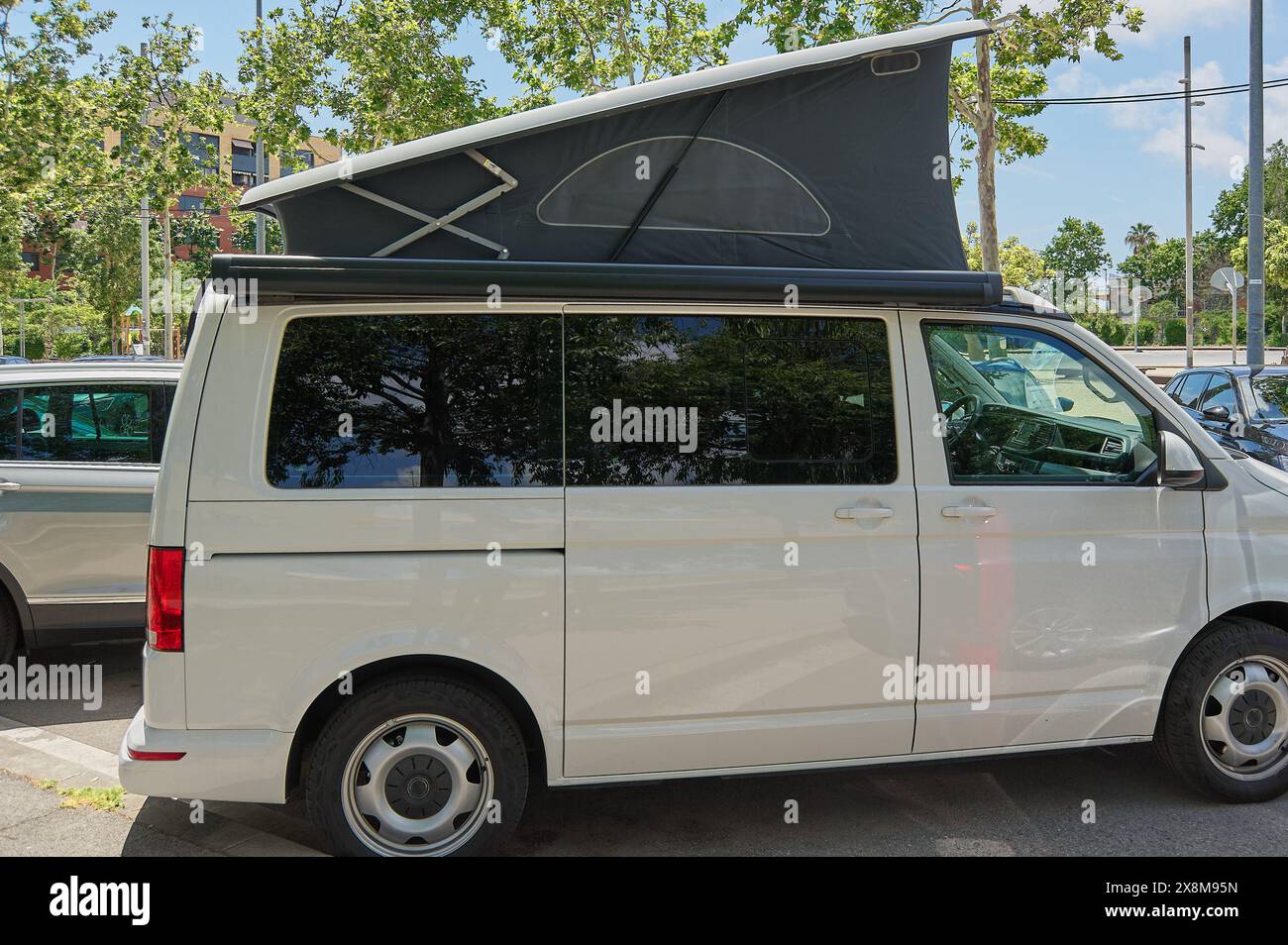 Fourgon de voyage blanc avec toit extensible garé dans un cadre urbain, parfait pour les aventures en plein air et le camping en ville. Banque D'Images