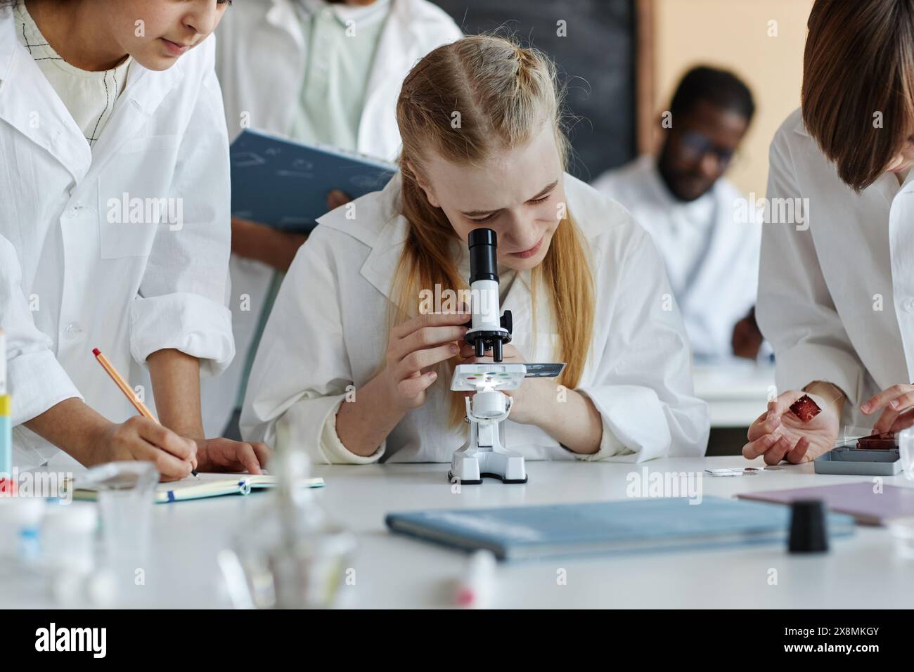Cliché sélectif d'une jeune fille caucasienne au microscope en faisant une expérience chimique avec des camarades de classe pendant la leçon Banque D'Images