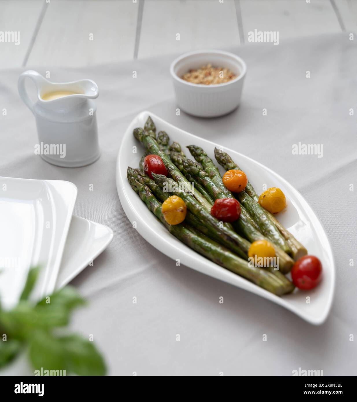 Une source de grandes fibres alimentaires, asperges vertes cuites au four servies dans une assiette blanche, comme plat d'accompagnement avec tomates colorées et sauce hollandaise Banque D'Images