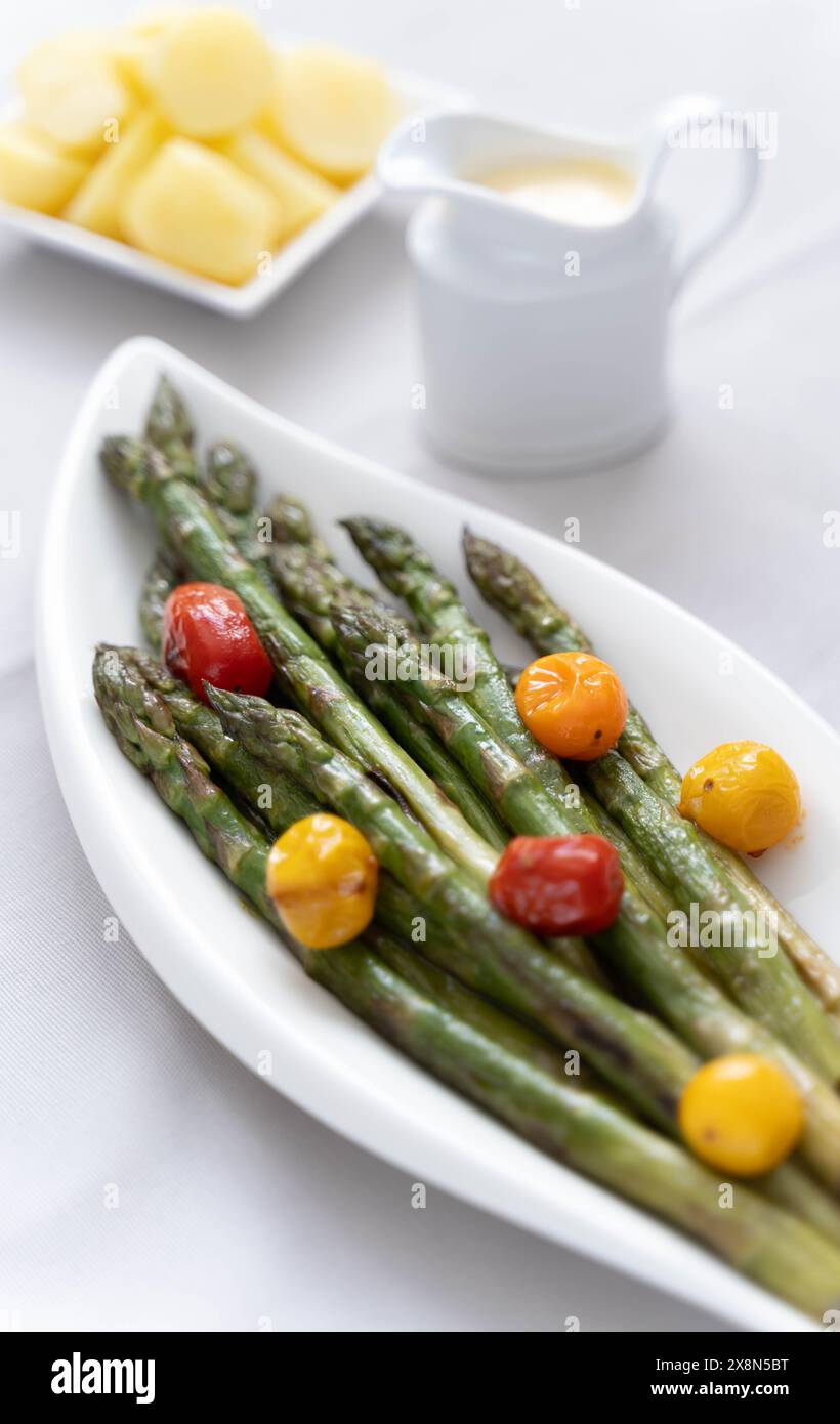 Une source de grandes fibres alimentaires, asperges vertes cuites au four servies dans une assiette blanche, préparées comme plat d'accompagnement avec des tomates colorées Banque D'Images