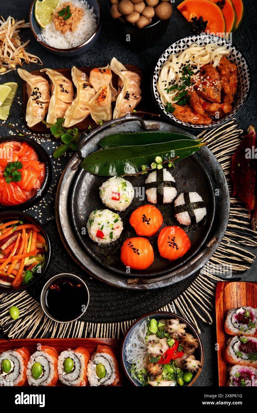 Sushi et cuisine japonaise sur un fond sombre. Rouleaux de sushi, soupe, riz frit, nigiri, sauce soja, baguettes. Cadre alimentaire asiatique/japonais. Vue de dessus. Banque D'Images