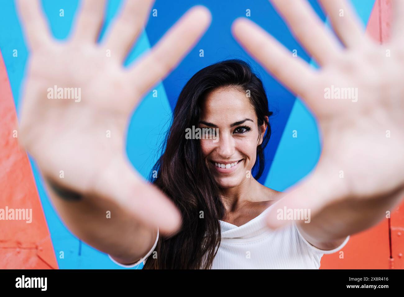 Femme souriante appuyée contre un mur tout en encadrant le visage avec les mains Banque D'Images