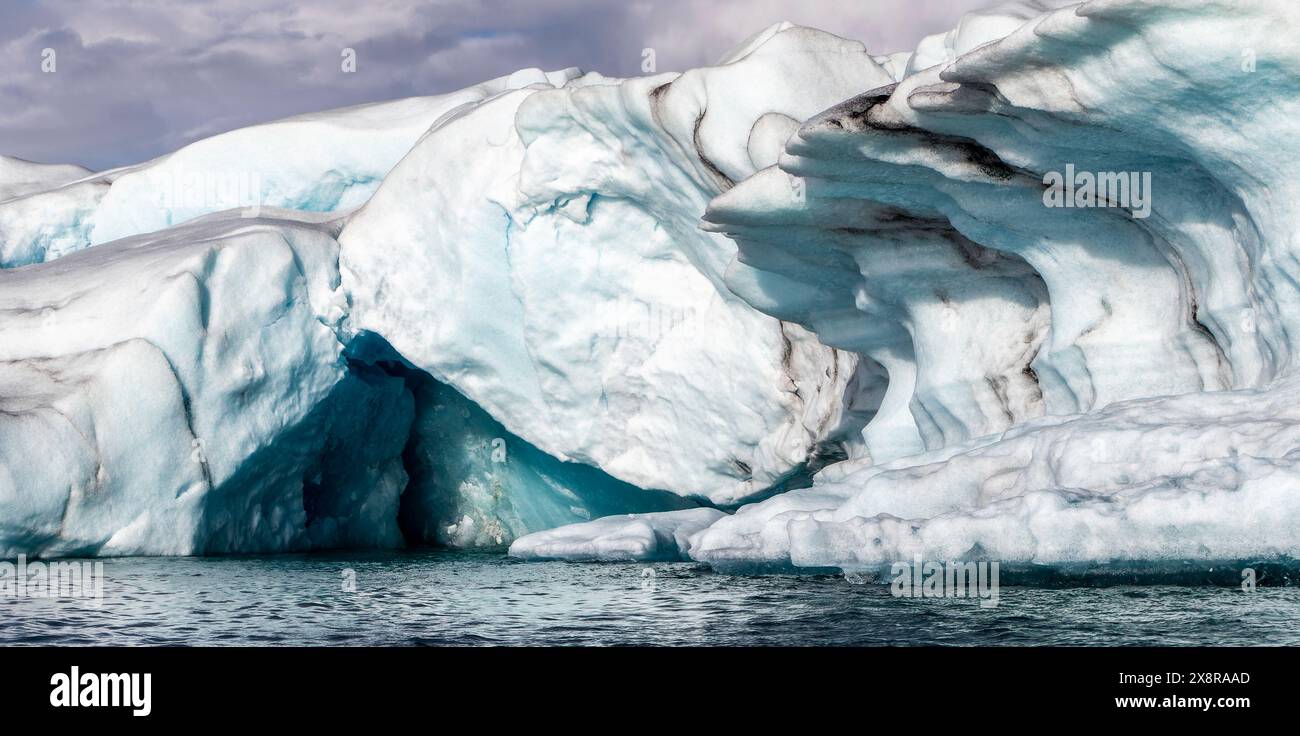 Un grand bloc de glace avec un trou dedans. La glace est bleue et blanche. L'eau est calme Banque D'Images