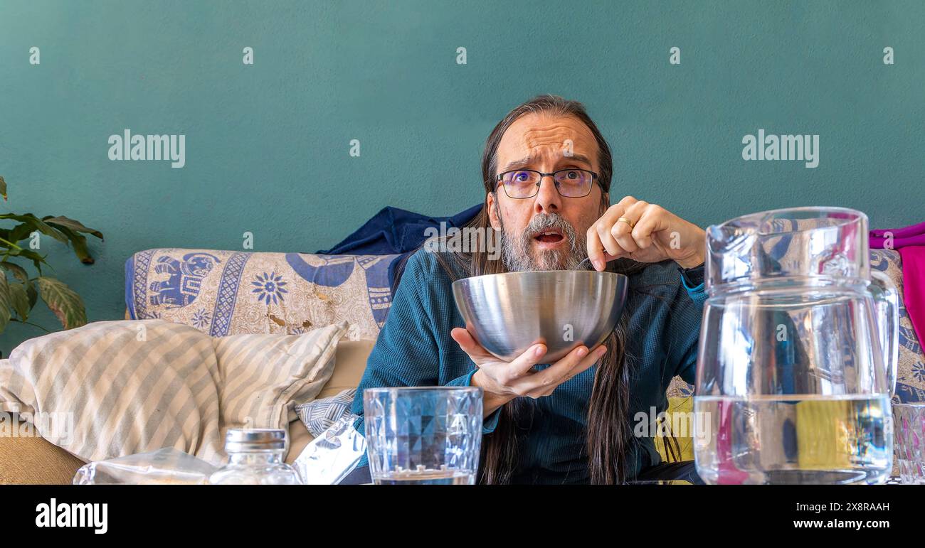 Un homme mange dans un bol en regardant avec intérêt quelque chose devant lui. L'homme semble totalement absorbé par ce qu'il voit. La scène est casu Banque D'Images