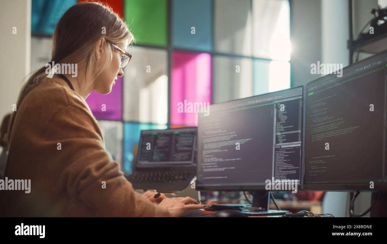 Ingénieur logiciel écrivant des lignes de code sur un PC professionnel à écrans multiples dans un bureau élégant. Femme caucasienne corrigeant les bugs et créant de nouvelles fonctionnalités pour un service numérique innovant. Banque D'Images