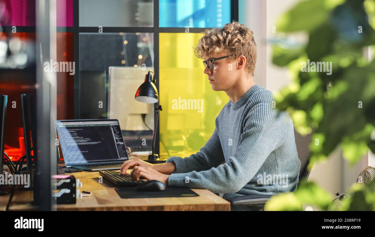 Vue latérale d'un stagiaire masculin en science des données écrivant des lignes de code sur un ordinateur de bureau dans un bureau élégant. Jeune homme caucasien résolvant des problèmes logiciels pour Big Tech Company. Le programmeur Fututre apprend le codage. Banque D'Images