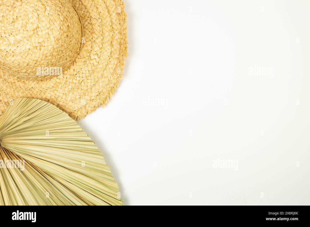 Vue de dessus du chapeau de paille et de la feuille de palmier séchée sur fond blanc. Mode d'été, vacances et fond d'écran de plage. Espace de copie, pose à plat. Banque D'Images