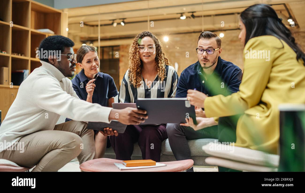 Groupe multiethnique de personnes créatives travaillant sur projet dans un bureau lumineux moderne. Un groupe diversifié de collègues développant une nouvelle approche à l'aide de graphiques, d'ordinateurs portables et de tablettes. Grand angle Banque D'Images