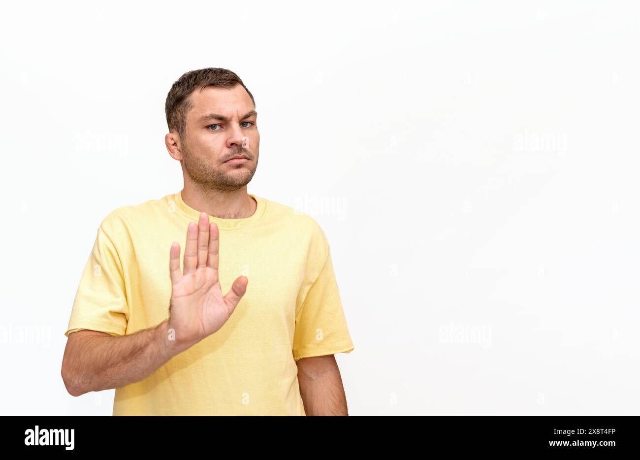 Personne masculine portant un t-shirt jaune se tient sur fond blanc et faisant un geste de refus, d'arrêt ou de non. Banque D'Images