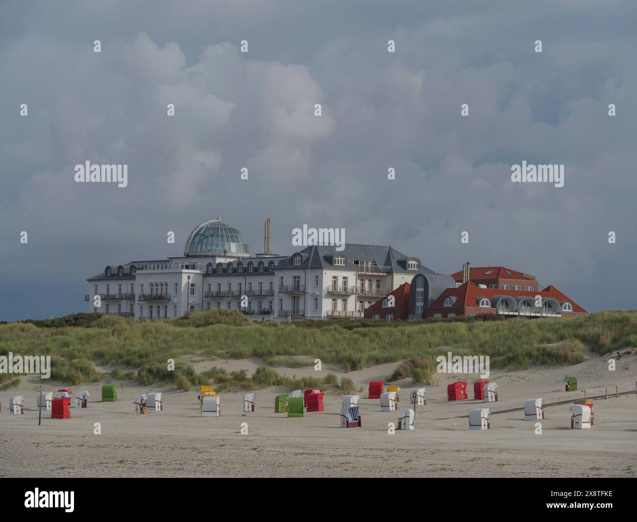 Plage avec chaises de plage colorées devant un grand bâtiment et ciel nuageux, plage avec chaises de plage colorées et dunes herbeuses au bord de la mer, Juist Banque D'Images