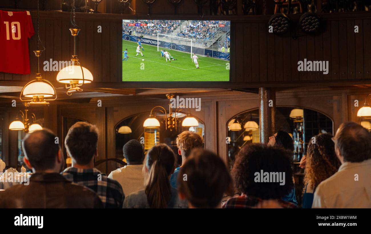 Groupe d'amis regardant un match de football en direct à la télévision dans un bar sportif. Fans excités acclamant et criant. Jeunes célébrant quand l'équipe marque un but et remporte la Coupe du monde de football. Banque D'Images