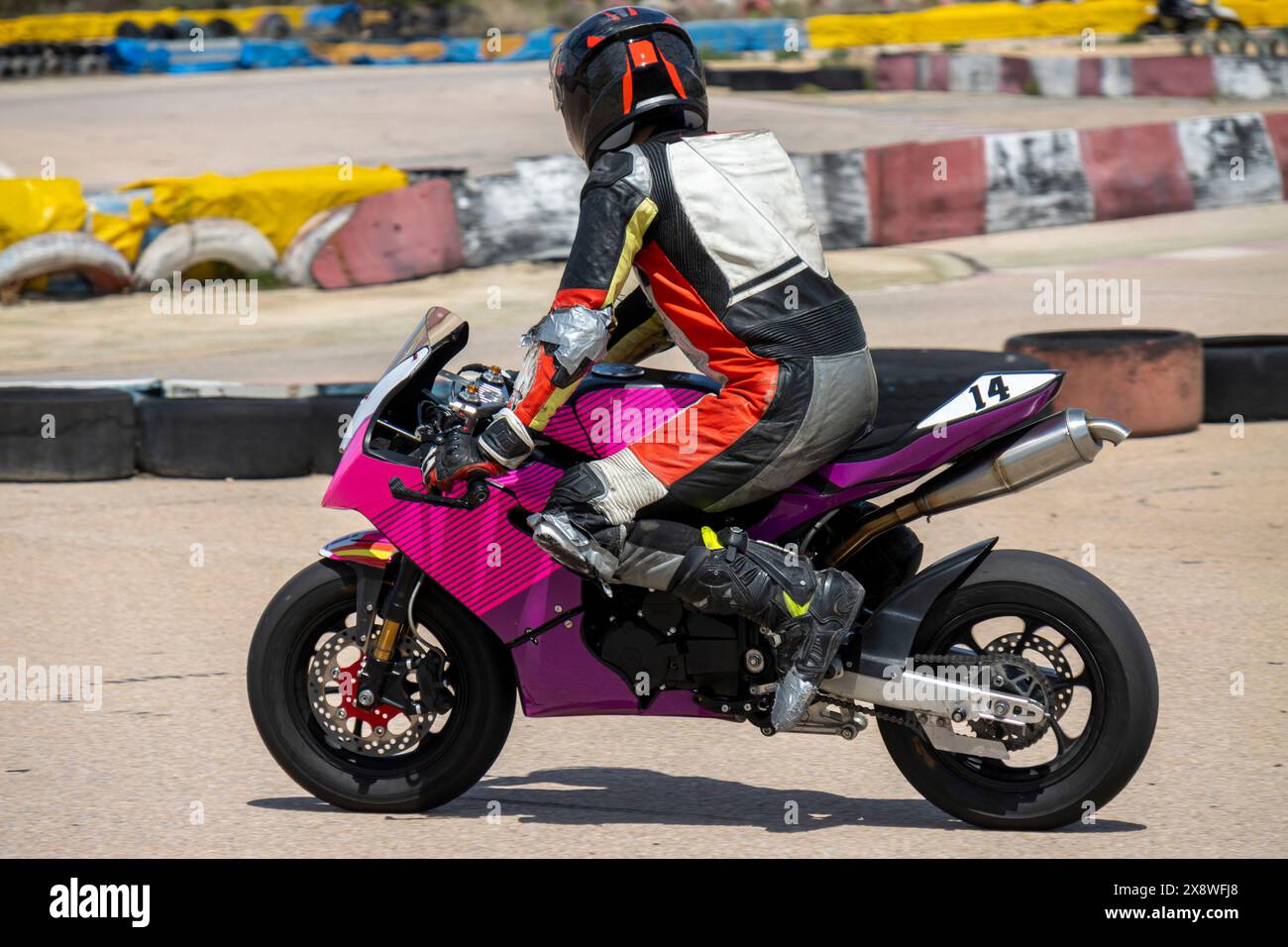 Pilote de moto dans l'équipement coloré monte un vélo de sport rose sur la piste, axé sur la course. Banque D'Images