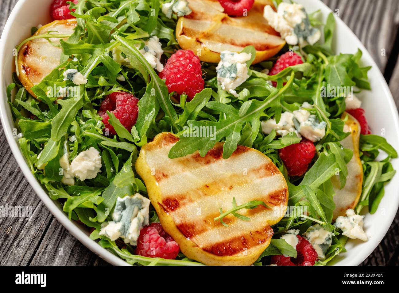 salade de poires grillées avec fromage bleu, roquette et framboises fraîches mûres dans un bol blanc sur une table en bois rustique, vue d'angle hollandais, gros plan Banque D'Images