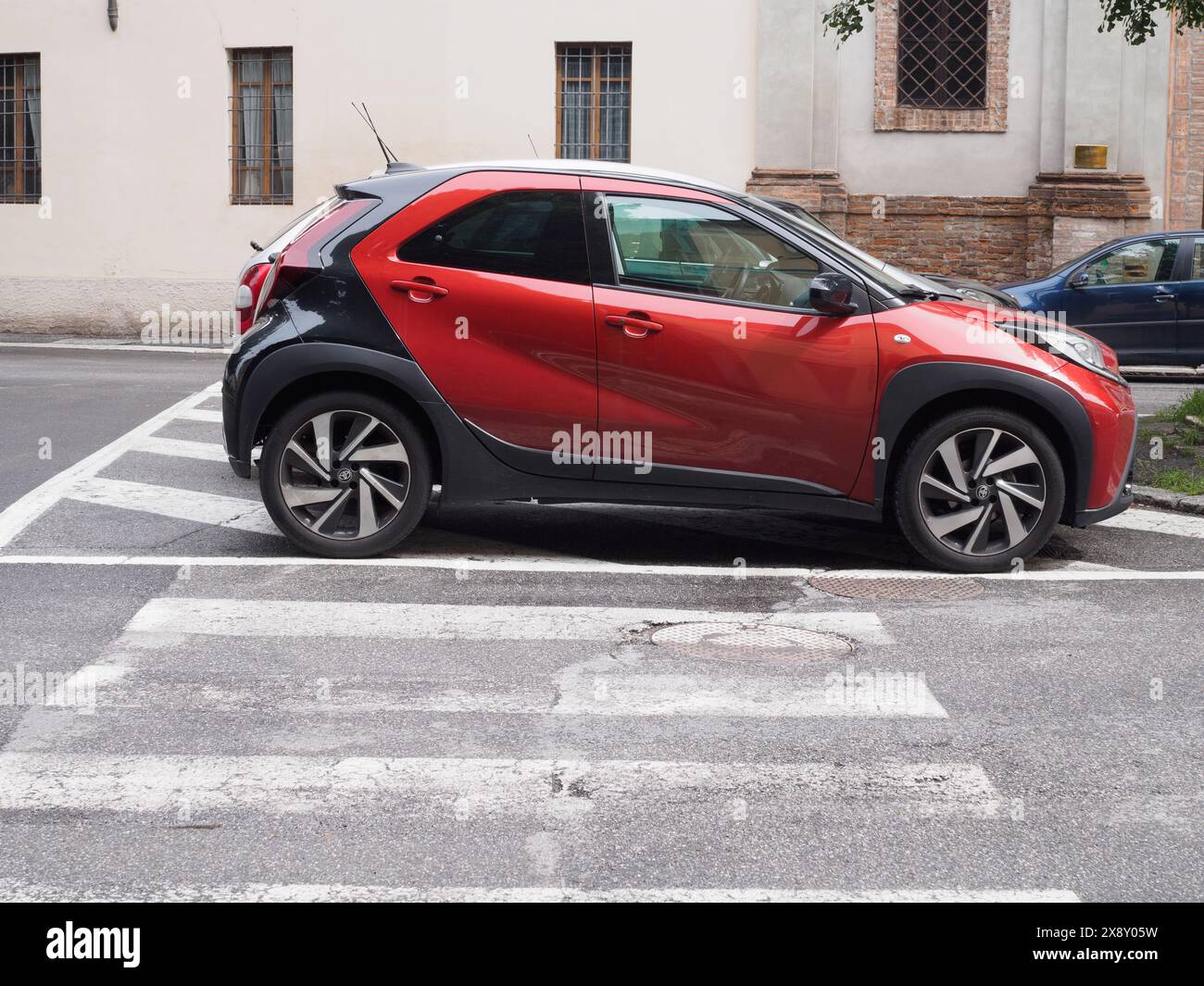 Cremona, Italie - 15 mai 2024 vus crossover compact Toyota Aigo rouge garé à côté d'un croisement zèbre dans une rue urbaine, avec des bâtiments et des voitures dans le Banque D'Images