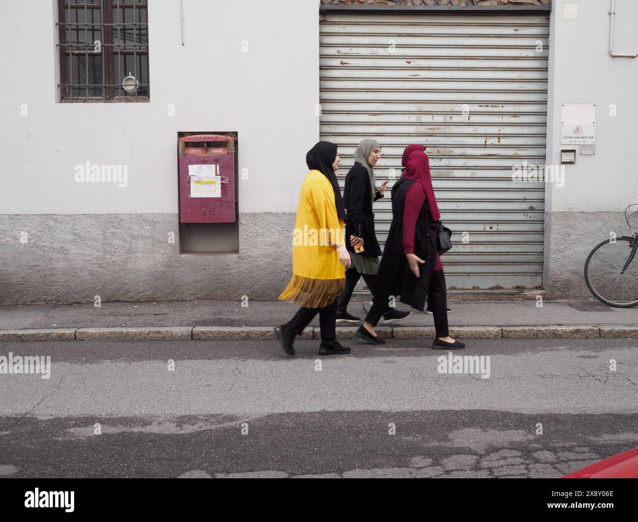 Cremona, Italie - 15 mai 2024 trois femmes musulmanes portant une robe traditionnelle marchant par une façade fermée avec volet métallique, mettant en valeur tous les jours c Banque D'Images