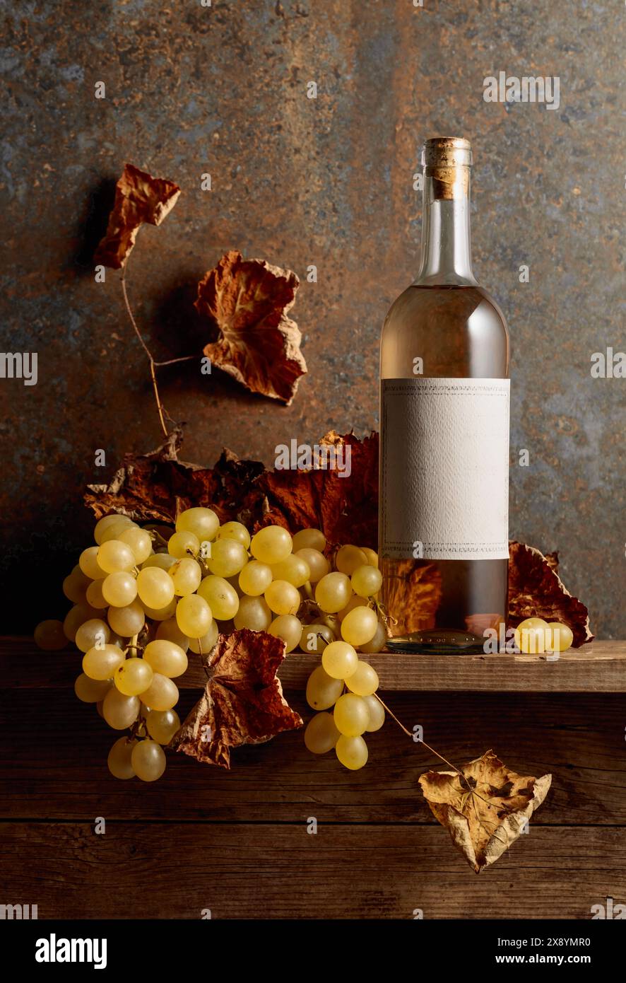 Bouteille de vin blanc avec des raisins et des feuilles de vigne séchées. Bouteille avec ancienne étiquette vide sur une table en bois. Copier l'espace. Banque D'Images