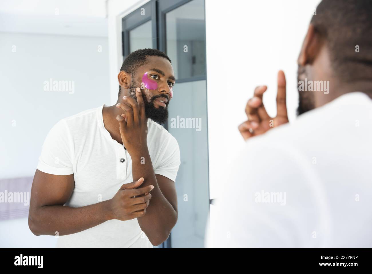 À la maison, homme afro-américain appliquant un masque facial, regardant dans un miroir Banque D'Images