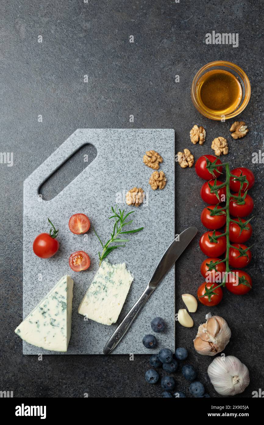 Vue de dessus de fromage à pâte molle avec moisissure bleue, miel, tomates cerises et ail sur planche à découper en pierre Banque D'Images