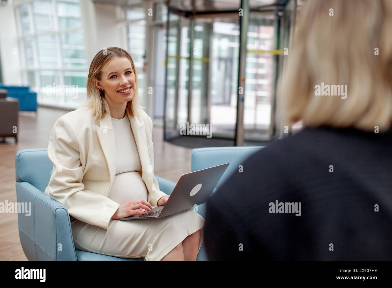 Femme enceinte en costume blanc lors d'une réunion d'affaires avec un collègue dans un espace de bureau moderne ou un centre de coworking. Femme d'affaires professionnelle multitâche Banque D'Images