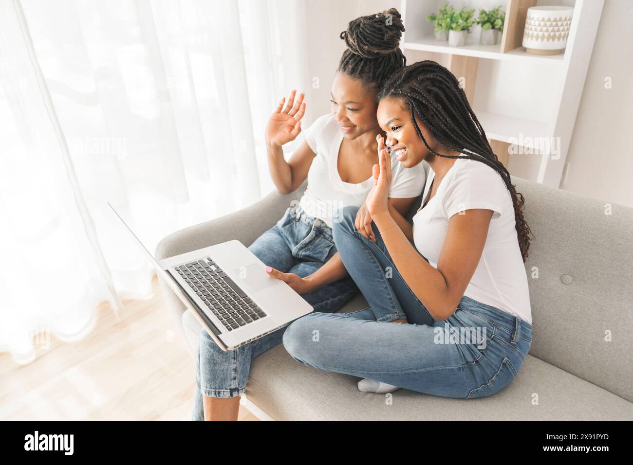 Mère et fille assis sur un canapé à la maison avec un ordinateur portable parlant avec un membre de la famille et dire bonjour Banque D'Images